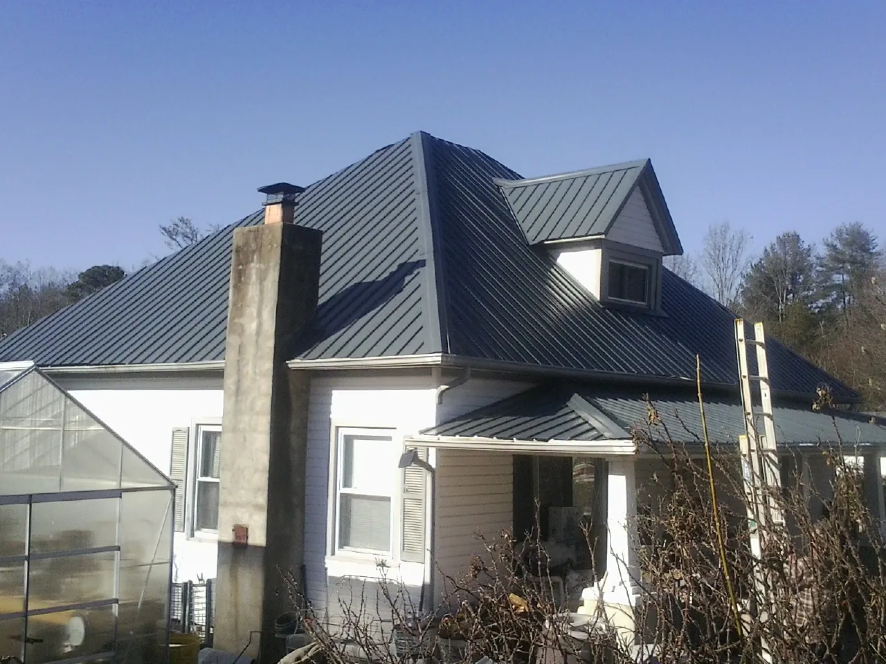Dark blue standing seam metal roof on a white farmhouse with dormer — Slate & Tile Roof Repair by Roofing Brothers in Littlerock