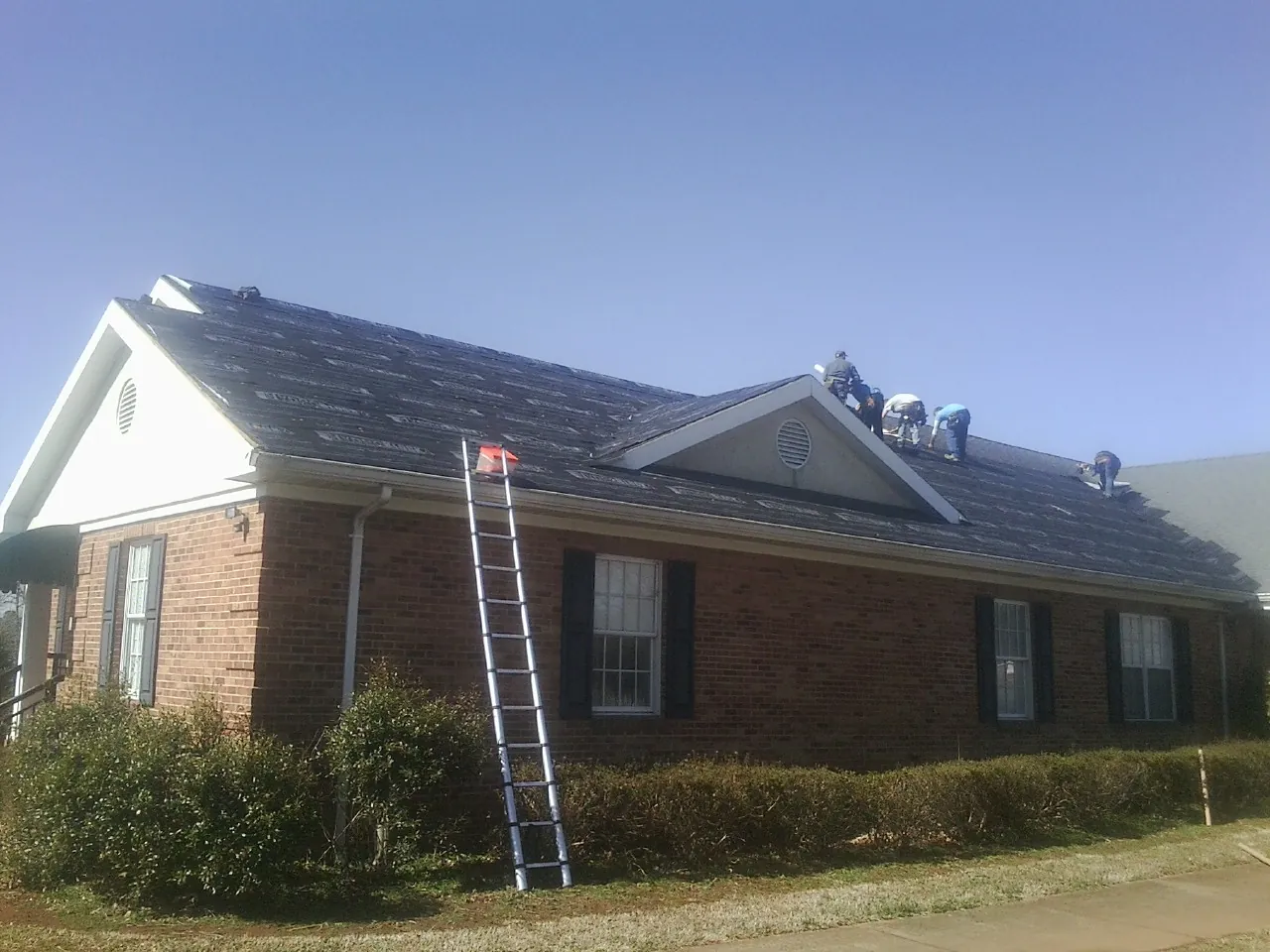 Crew tearing shingles off a brick ranch roof with a ladder set — Metal Roof Repair work by our crew in Littlerock