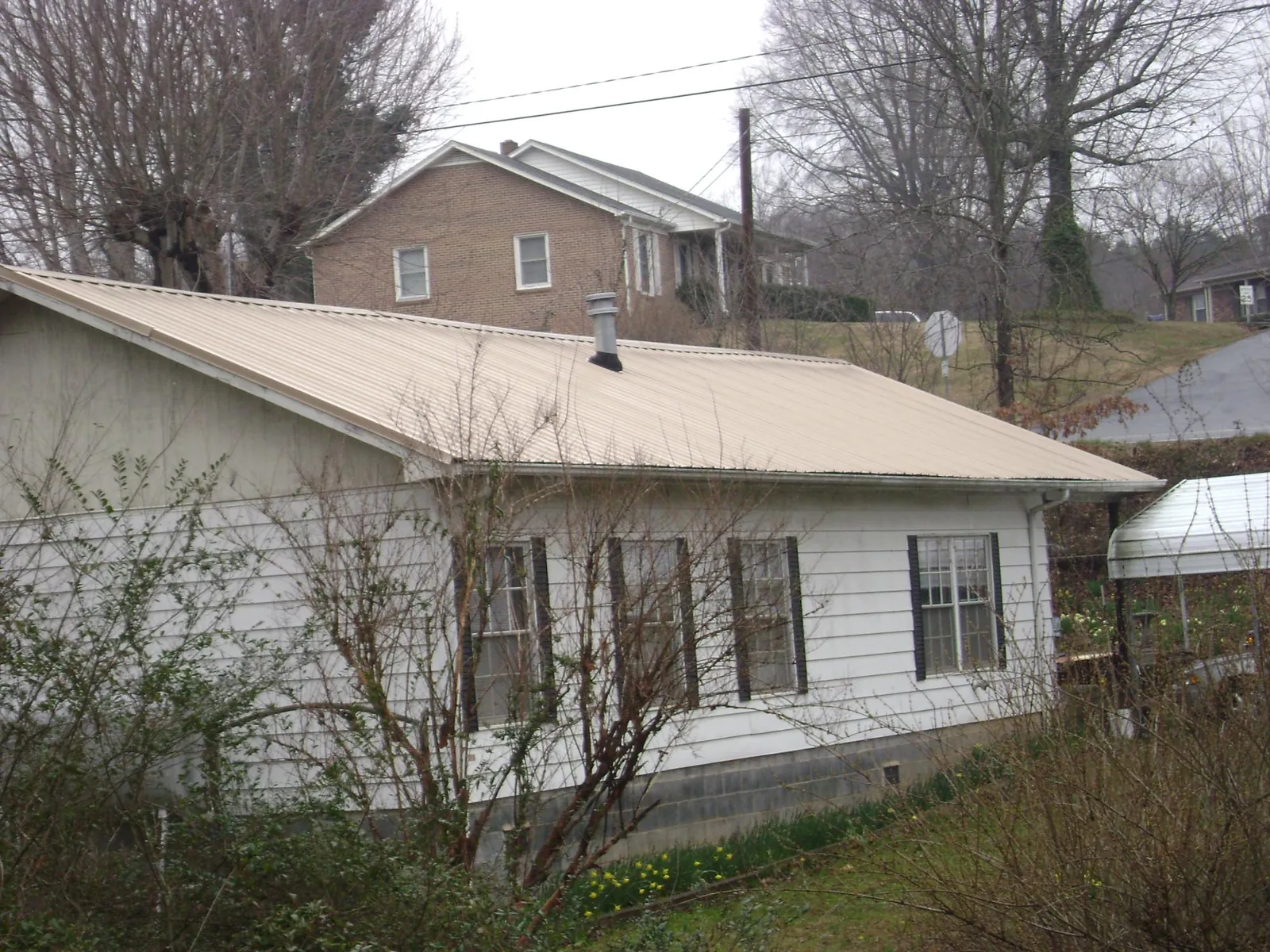 Tan metal roof on a white sided house set into a hillside — Commercial Roofing by Roofing Brothers in Littlerock